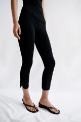 Pantalón capri negro de tiro medio con cintura elástica y detalle de alamares en el bajo.