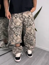 Pantalón baggy desmontable con estampado camuflado tipo Realtree de ramas y hojas en tonos beige y marrón, de corte holgado.