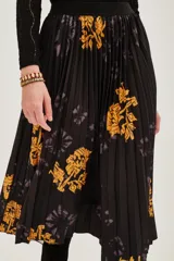 Falda midi plisada de color negro con estampado floral en tonos amarillos y detalles de efecto tie-dye. Presenta una silueta acampanada con movimiento y cintura elástica.