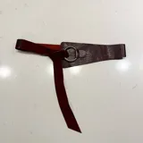 Cinto de cuero con textura tipo reptil en color bordó, con diseño de aro metálico en tono bronce y tira de ajuste en gamuza al tono.