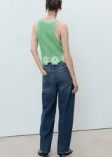 Top sin mangas verde de punto medio con cuello redondo y diseño recto. Presenta un detalle de bajo con acabado floral bordado y calado.