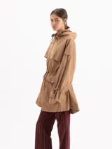 Piloto James de nylon liviano color marrón, con capucha envolvente, cintura ajustable con cordón y tancas, cierre frontal con cremallera y dos bolsillos delanteros con solapa y broches.