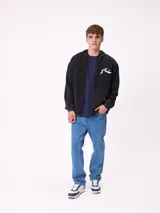 Canguro con capucha de color negro con efecto lavado, manga larga y bolsillo frontal. Presenta un estampado gráfico en la espalda con el logo de la marca y motivos abstractos en tonos violeta y amarillo.