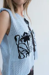 Chaleco de punto calado celeste con diseño estampado en negro y cierre frontal mediante tiras tejidas a crochet.