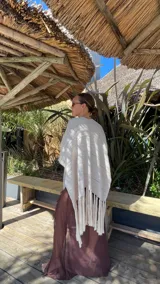 Ruana de tejido de punto color crema con diseño de líneas horizontales caladas y terminación con flecos en el ruedo.