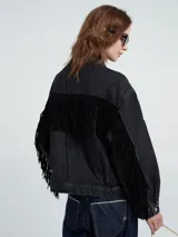Chaqueta de jean color negro, con diseño de corte holgado, cierre frontal con botones metálicos y detalle de flecos largos en las mangas y la parte trasera.