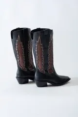 Bota texana de cuero negro con apliques de cuero marrón en los laterales y pespuntes en color crema. De caña media/alta y taco bajo. Diseño calado con motivos geométricos.
