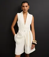 Chaleco sastre alargado color blanco hueso con finas rayas verticales. Presenta cuello tipo blazer, cierre cruzado con un botón metalizado y un lazo ancho para ajustar a la cintura.