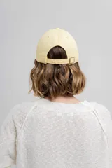 Gorra verde militar de diseño clásico con visera curva y aplique metálico plateado con la inscripción "Peach" en el lateral frontal. Cuenta con tira ajustable en la parte trasera.