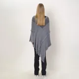 Poncho de tejido de punto gris con diseño asimétrico, detalles de flecos en los bordes y costuras decorativas con textura desflecada.