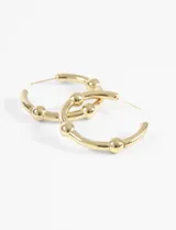 Aros tipo argolla de acero quirúrgico hipoalergénico color dorado, con bolitas decorativas.