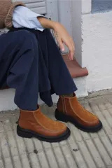 Bota corta de cuero color marrón con paneles en gamuza al tono, diseño de punta redondeada y suela track negra de goma. Presenta cierre lateral y detalle de costuras a la vista.