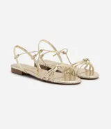 Sandalia plana marca Satinato, color dorado metalizado con textura tipo croco. Posee tiras finas con detalle de nudo en el empeine y cierre de lazo ajustable al tobillo. Diseño de puntera redonda y suela plana.