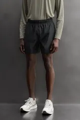 Short de running 2 en 1 color beige, confeccionado en tejido técnico ligero y elástico con malla interior integrada. Presenta cintura elástica ajustable con cordón, bolsillo trasero con cierre y aberturas laterales en el bajo.