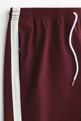 Short deportivo de nylon color bordó, con franjas laterales blancas, cintura elástica con cordón de ajuste blanco y bolsillos laterales.