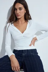 Top de manga larga blanco con escote en V y detalle de nudo fruncido en el centro del pecho.