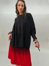 Blusa negra de lana y poliéster, liviana y sutilmente transparente, con terminación asimétrica y tablas que le brindan volumen y movimiento. Presenta dos lazos delanteros que permiten ajustar a gusto adelante y/o atrás.