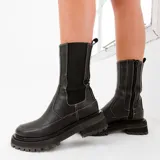 Bota corta tipo chelsea de cuero vacuno color negro, con suela de goma track, cierre lateral interno y elástico lateral externo.