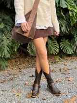 Botas de cuero color chocolate, de caña alta con detalle de hebillas y tachas.