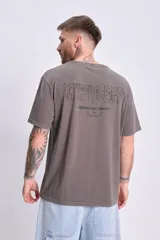 Remera de manga corta gris oscuro, corte oversize, con estampado frontal que incluye un logo con tipografía futurista, un globo terráqueo y un emoticón.