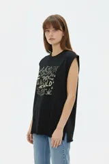 Musculosa color crudo con estampado frontal de paisaje montañoso y texto "EXPLORING Outlands", corte holgado y aberturas laterales en el ruedo.