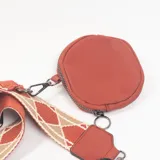 Bandolera color ladrillo con cierre principal, correa ancha ajustable con diseño geométrico y monedero circular extraíble a juego.