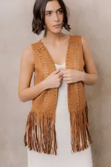Chaleco de efecto gamuza en tono camel, sin mangas, con escote en V y diseño abierto. Presenta detalles de tachas metálicas, entramado artesanal en el frente y flecos largos en el ruedo.