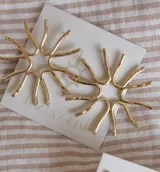 Caravanas de diseño circular con forma de sol, elaboradas en metal dorado con acabado texturizado.