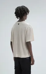 Remera de tejido de punto color beige con moldería ligeramente oversize, cuello redondo y mangas cortas. Confeccionada en una mezcla de viscosa y poliéster que ofrece una caída fluida y textura suave.