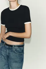 Camiseta blanca de manga corta y cuello redondo, con ribete negro decorado con perlas blancas en el cuello y los puños.