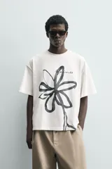 Camiseta de corte relajado confeccionada en algodón, con cuello redondo y manga corta. Presenta un estampado artístico de una flor a trazo grueso en color negro sobre fondo blanco.