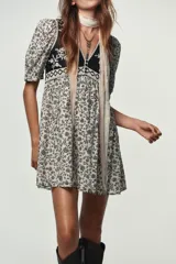 Vestido corto con estampado floral en blanco y negro, escote pico, mangas cortas abullonadas y detalle de chaleco negro con bordados y falsos botones delanteros. Incluye forro interior.