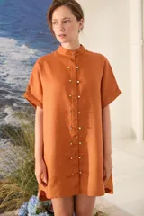 Vestido corto color beige de lino, con moldería amplia, manga corta, cuello mao y cierre frontal con botones dorados.