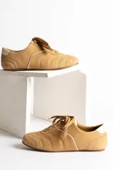 Zapatillas bajas color crema con cordones y suela marrón.