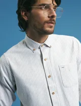 Camisa de manga larga con estampado de rayas verticales finas en tonos gris y blanco. Presenta cuello button-down, bolsillo frontal en el pecho y botones de madera.