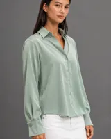 Camisa de satén color verde pistacho, con cuello clásico, cierre frontal de botones y mangas largas con puños abotonados.