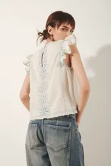 Camisa sin mangas color blanco roto, con volados en los hombros y bordado estilo calado en el frente con motivos florales en hilo celeste.