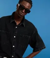 Camisa masculina de jeans negro con lavado marmolado, corte boxy, cuello inglés, manga corta, abotonada al frente y con dos bolsillos de parche en el pecho.