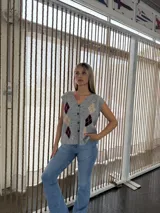 Chaleco de punto gris con escote en V, cierre frontal de botones y diseño de rombos en tonos bordó y beige.