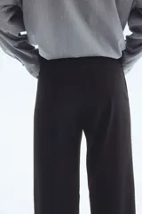 Pantalón negro de vestir, tiro alto, con piernas anchas y corte recto. Presenta pliegues marcados en el frente y cierre frontal oculto.