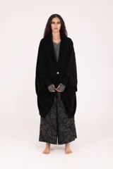 Saco negro de silueta amplia y caída relajada, con solapas y cierre frontal mediante un botón plateado. Presenta un calce recto y largo por debajo de la cadera.