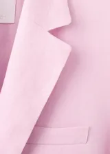 Blazer de lino color rosado, de diseño recto con cuello en pico y solapas con muesca. Cuenta con manga larga, dos bolsillos de ribete delanteros y cierre frontal de un botón.