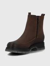 Bota tipo Chelsea de cuero marrón con paneles laterales elásticos en color negro. Presenta costuras reforzadas en el contorno y una suela robusta de poliuretano con base dentada en tono gris translúcido.
