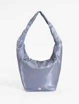 Bolso tipo hobo de color negro con acabado satinado y estructura blanda. Cuenta con un asa corta integrada, cierre superior y un llavero decorativo con temática de tenis colgando del tirador del cierre.