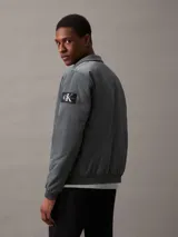 Campera bomber gris de nailon reciclado, con cuello alto, cierre de cremallera, bolsillos laterales y puños y bajo elásticos.