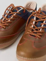 Championes urbanos de cuero con diseño de paneles en color negro y marrón. Presentan cordones trenzados, costuras a la vista y detalle de refuerzo en el talón con pespuntes decorativos.