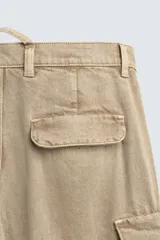 Pantalón cargo de denim lavado negro, corte relajado y tiro medio. Presenta múltiples bolsillos cargo con solapa y detalle de cierre en las perneras, además de bolsillos de vivo traseros. El bajo es ajustable con trabilla.