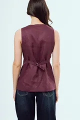 Top estilo chaleco sin mangas, de color bordó, con cuello redondo y cierre frontal con botones oscuros. Presenta bolsillos ojal simulados en la parte inferior del frente.