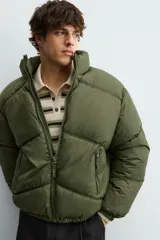 Cazadora acolchada tipo puffer de corte relajado, color verde militar. Presenta cuello subido, cierre frontal con cremallera, bolsillos laterales con cierre y puños elásticos.