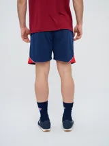Bermuda deportiva Umbro del Club Nacional de Football, modelo Nexo para hombre, en color azul marino con detalles en rojo y blanco. Cuenta con el escudo del club bordado en la pierna derecha y el logo de Umbro en la izquierda, además de cordón ajustable en la cintura.